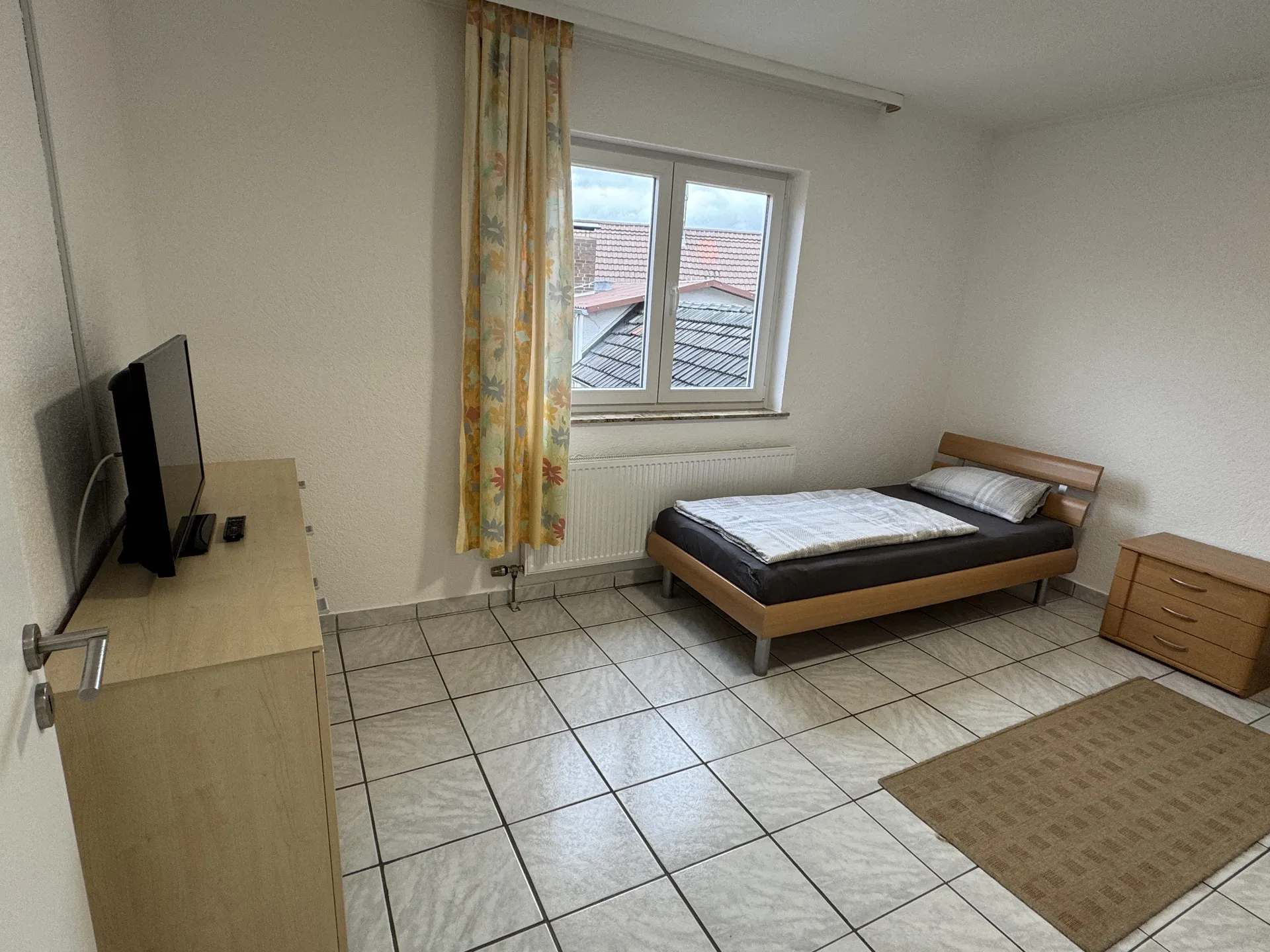 Einzelzimmer der Handwerkerunterkunft in Butzbach mit Bett, Kommode und TV am Fenster